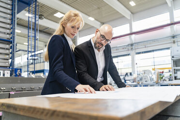 Businessman and businesswoman looking at plan on table in factory - DIGF06089