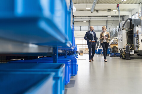 Geschäftsmann und Geschäftsfrau gehen und sprechen in einer Fabrik, lizenzfreies Stockfoto