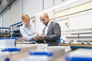 Businessman and businesswoman examining workpiece in factory - DIGF06121