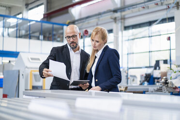 Geschäftsmann und Geschäftsfrau sehen sich Papier in einer Fabrik an - DIGF06146