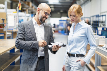 Businessman and businesswoman examining workpiece in factory - DIGF06173