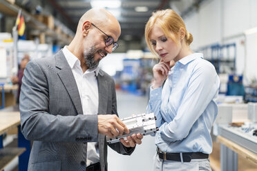 Businessman and businesswoman examining workpiece in factory - DIGF06174