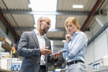 Businessman and businesswoman examining workpiece in factory - DIGF06175