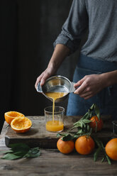 Young man pouring freshly squeezed orange juice into a glass, partial view - ALBF00780