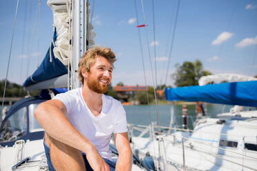 Young man sitting on sailboat on Chiemsee lakeside, Bavaria, Germany - CUF49624