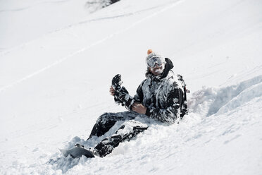 Männlicher Snowboarder, bedeckt mit Schnee, sitzend am Berghang, Alpe-d'Huez, Rhone-Alpes, Frankreich - CUF49687