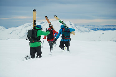 Landschaft mit drei männlichen Skifahrern, die in Richtung Berg stapfen, Rückansicht, Alpe-d'Huez, Rhone-Alpes, Frankreich - CUF49707