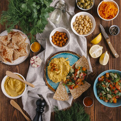 Overhead view of hummus with flatbread and salad in plate amidst ingredients on table - CAVF63004