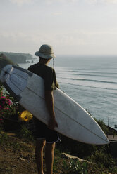 Junger Mann schaut auf das Meer und hält ein Surfbrett auf einem Berg - CAVF63011