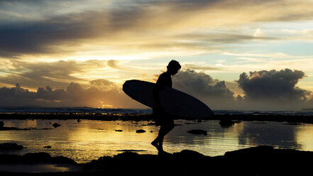 Seitenansicht von Silhouette Tourist mit Surfbrett zu Fuß am Strand gegen bewölkten Himmel bei Sonnenuntergang - CAVF63016