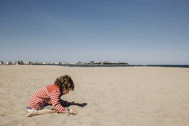 Seitenansicht des Jungen spielt mit Sand am Strand gegen den Himmel während des sonnigen Tages - CAVF63017