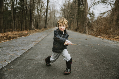 Porträt eines niedlichen Jungen in voller Länge, der mit einem Stock auf der Straße spielt - CAVF63019