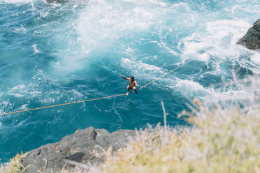 Hoher Blickwinkel eines jungen Mannes, der Slacklining über dem Meer übt - CAVF63028