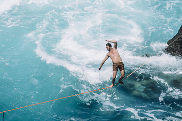 Unbeschwerter junger Mann beim Slacklinen auf einem Seil über dem Meer an einem sonnigen Tag - CAVF63030