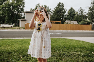 Porträt eines niedlichen Mädchens, das eine Tiara trägt, während es auf einem grasbewachsenen Feld im Hof steht - CAVF63108
