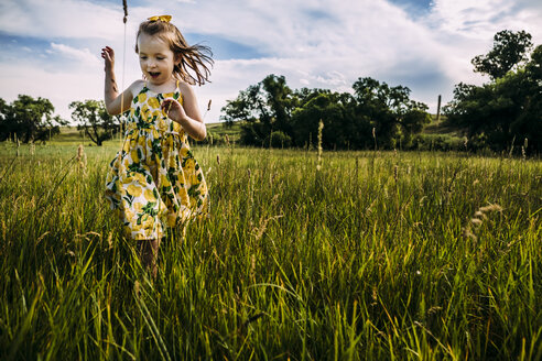 Nettes Mädchen geht auf grasbewachsenem Feld gegen bewölkten Himmel - CAVF63115
