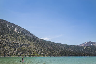 Mother paddleboarding with daughter in lake against mountains and sky during summer - CAVF63121