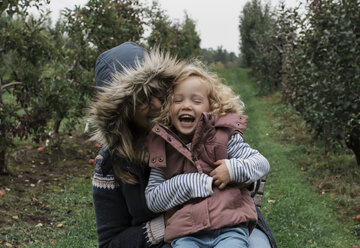 Happy mother with daughter sitting on grassy field in forest - CAVF63140