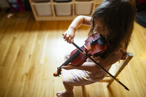 Hohe Winkel Ansicht des Mädchens spielt Geige, während auf Stuhl zu Hause sitzen, lizenzfreies Stockfoto