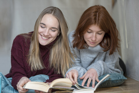 Zwei Freunde liegen Seite an Seite auf dem Boden und lesen Bücher, lizenzfreies Stockfoto