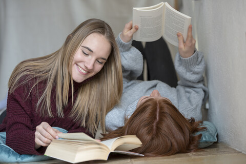 Two friends lying side by side on the floor reading books stock photo