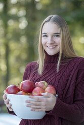 Porträt einer lächelnden blonden jungen Frau, die eine Schale mit Äpfeln hält - LBF02412