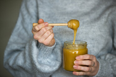 Hands of teenage girl holding honey jar and honey dipper, close-up - LBF02420