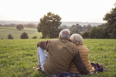 Back view of senior couple sitting on a meadow enjoying sunset - MAMF00481