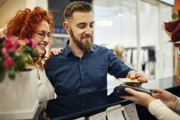 Happy couple paying at counter in flower shop - ZEDF01990