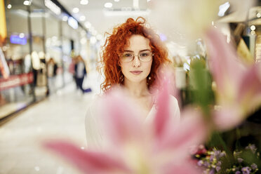 Portrait of redheaded woman behind blossom in a shopping arcade - ZEDF02011