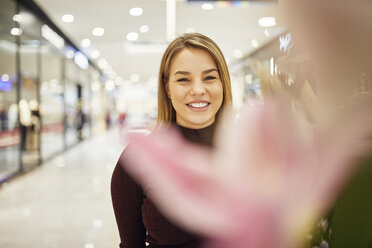 Porträt einer lächelnden Frau hinter einer Blüte in einer Einkaufspassage - ZEDF02012