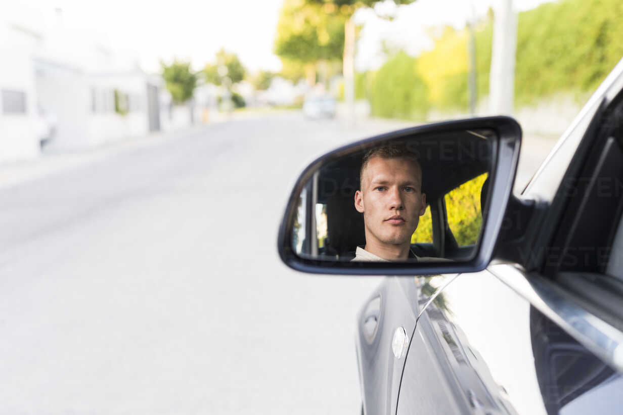 Spiegelung eines jungen Mannes im Außenspiegel eines Autos