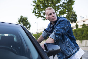 Junger Mann in Jeansjacke lehnt an Auto - ABZF02252