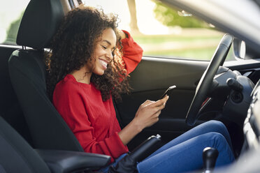 Lächelnde junge Frau, die in einem Auto ein Handy benutzt - JSMF00804