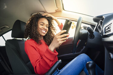 Glückliche junge Frau, die im Auto ein Mobiltelefon benutzt - JSMF00805