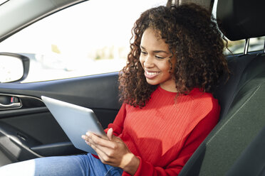 Lächelnde junge Frau, die in einem Auto ein Tablet benutzt - JSMF00807