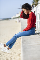 Glückliche junge Frau auf der Strandpromenade sitzend - JSMF00808