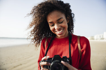 Lächelnde junge Frau schaut in die Kamera am Strand - JSMF00825