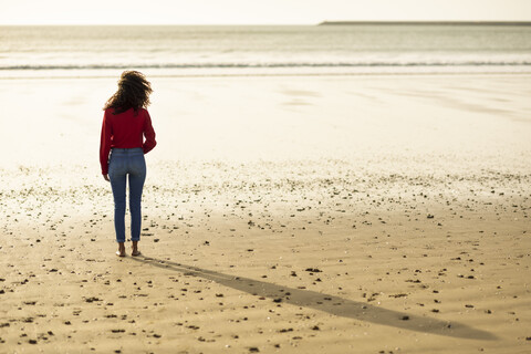 Rückansicht einer jungen Frau, die bei Sonnenuntergang am Strand steht, lizenzfreies Stockfoto