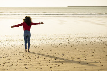 Rückansicht einer jungen Frau, die bei Sonnenuntergang am Strand steht - JSMF00827