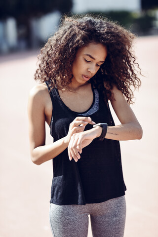 Sportliche junge Frau schaut im Freien auf ihre Smartwatch, lizenzfreies Stockfoto