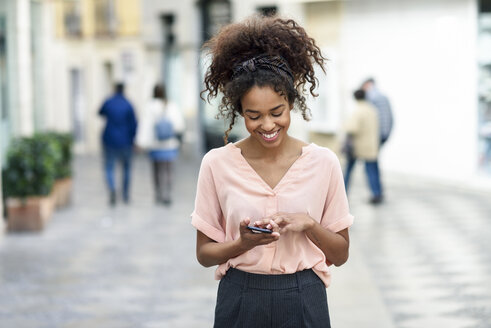 Smiling young woman using cell phone in the city - JSMF00849