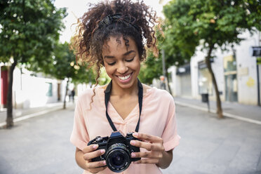 Lächelnde junge Frau mit Blick in die Kamera in der Stadt - JSMF00863
