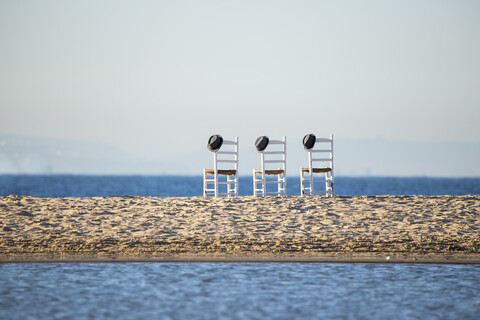 Drei leere Stühle mit Hüten nebeneinander vor dem Meer, lizenzfreies Stockfoto