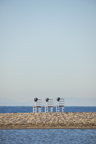 Three empty chairs with hats side by side in front of the sea stock photo