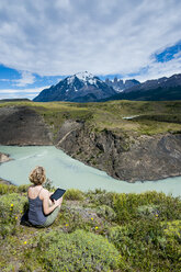 Chile, Patagonien, Frau mit Tablet an einer Flussbiegung im Torres del Paine National Park - RUNF01479