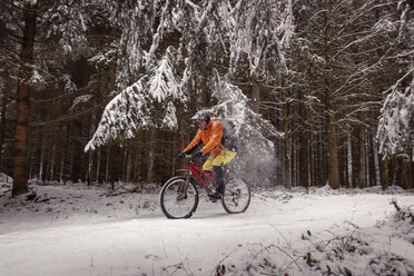 Mann fährt Mountainbike auf einem Weg im Winterwald - SEBF00044