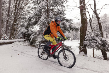 Mann fährt Mountainbike auf einem Weg im Winterwald - SEBF00045