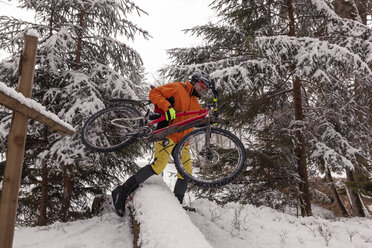 Mann mit Mountainbike überquert umgestürzten Baum auf Weg im Winterwald - SEBF00047