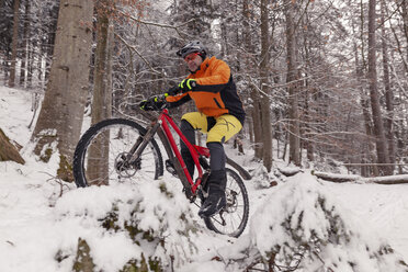 Mann fährt Mountainbike auf einem Weg im Winterwald - SEBF00048